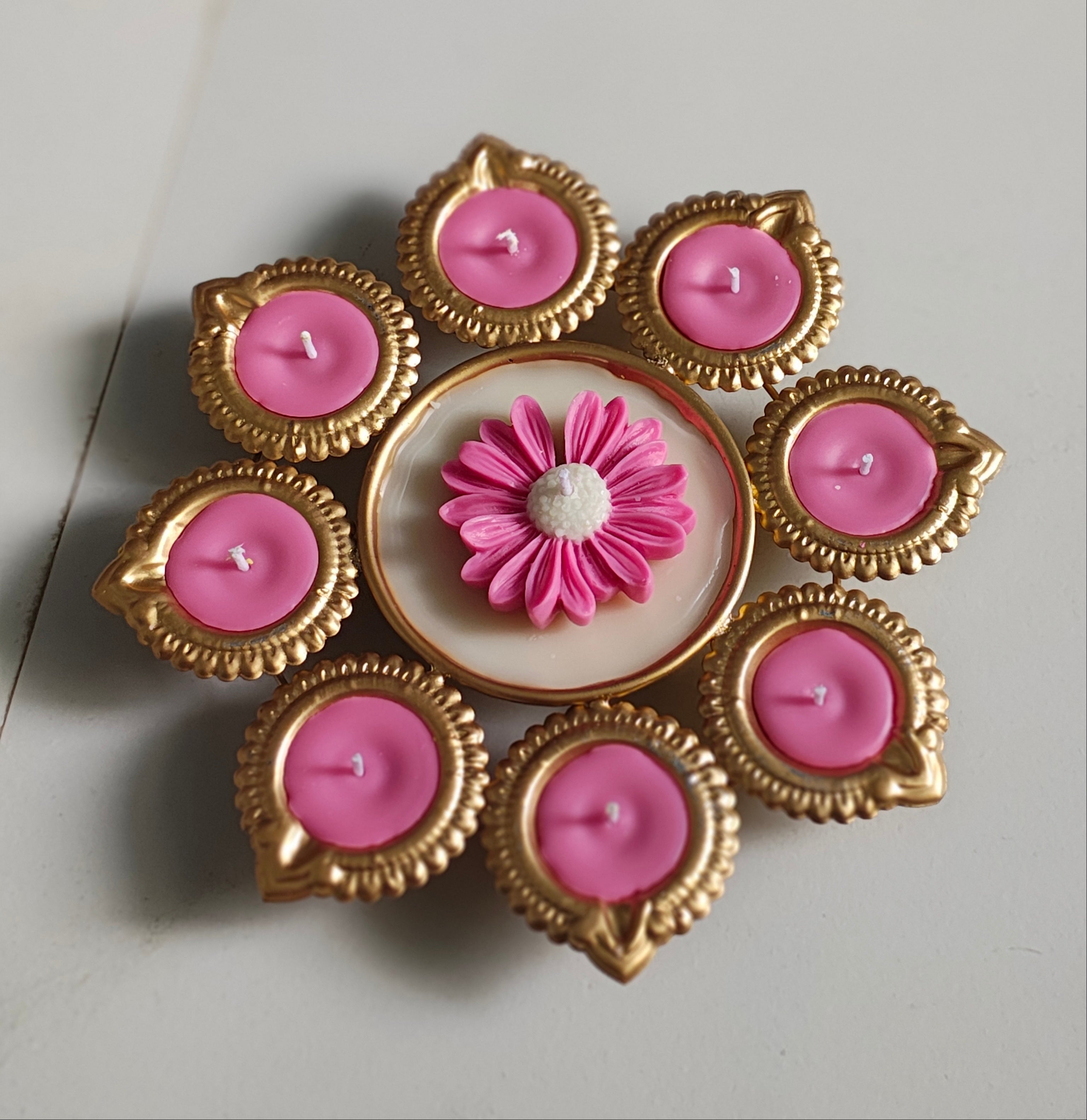 Decorative candle holder with pink candles and a central flower design on a light gray background